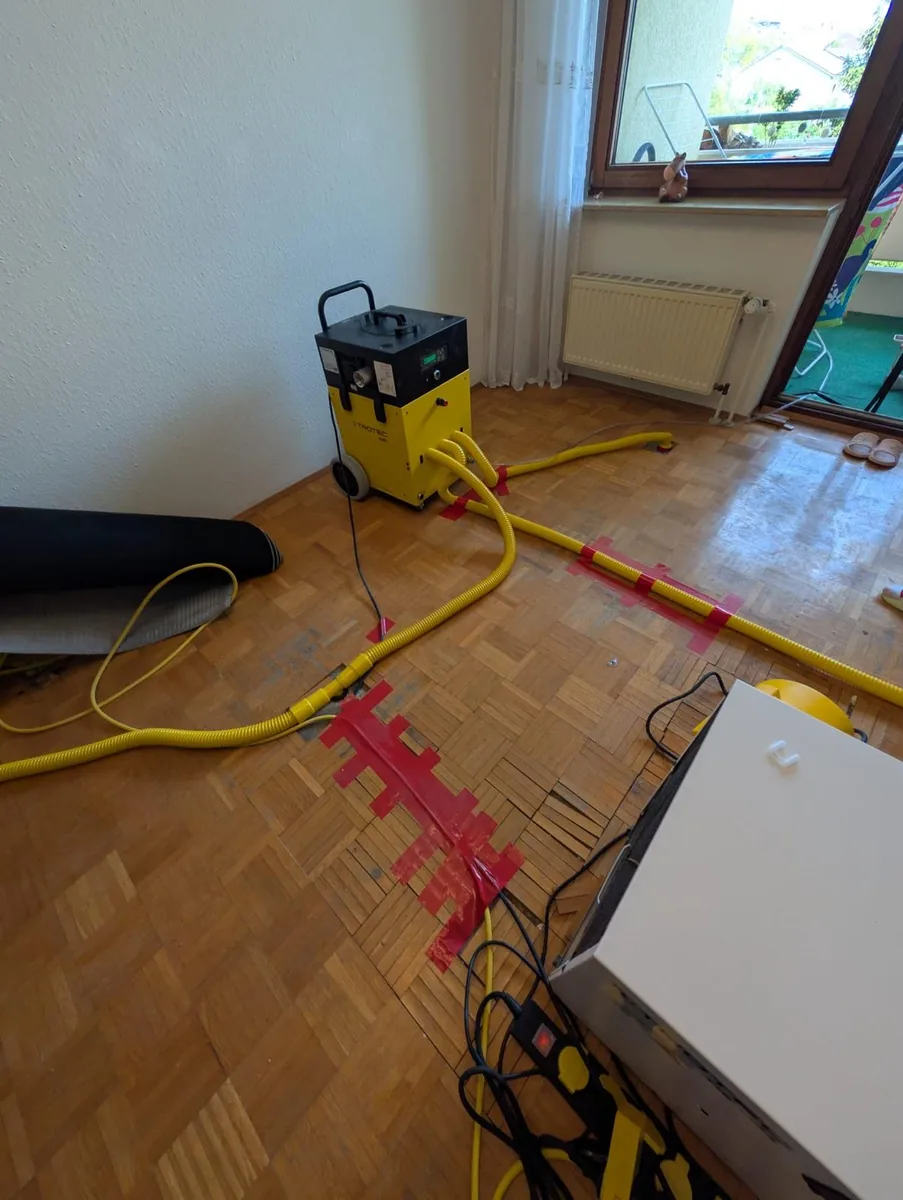 Dämmschichttrocknung: Trocknungsgeräte mit Schläuchen auf Parkettboden nach Wasserschaden